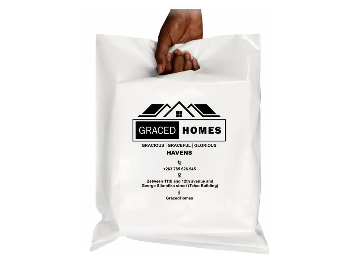 A hand holding a white Graced Homes boutique bag printed in black with the brand's rooftop logo and contact details