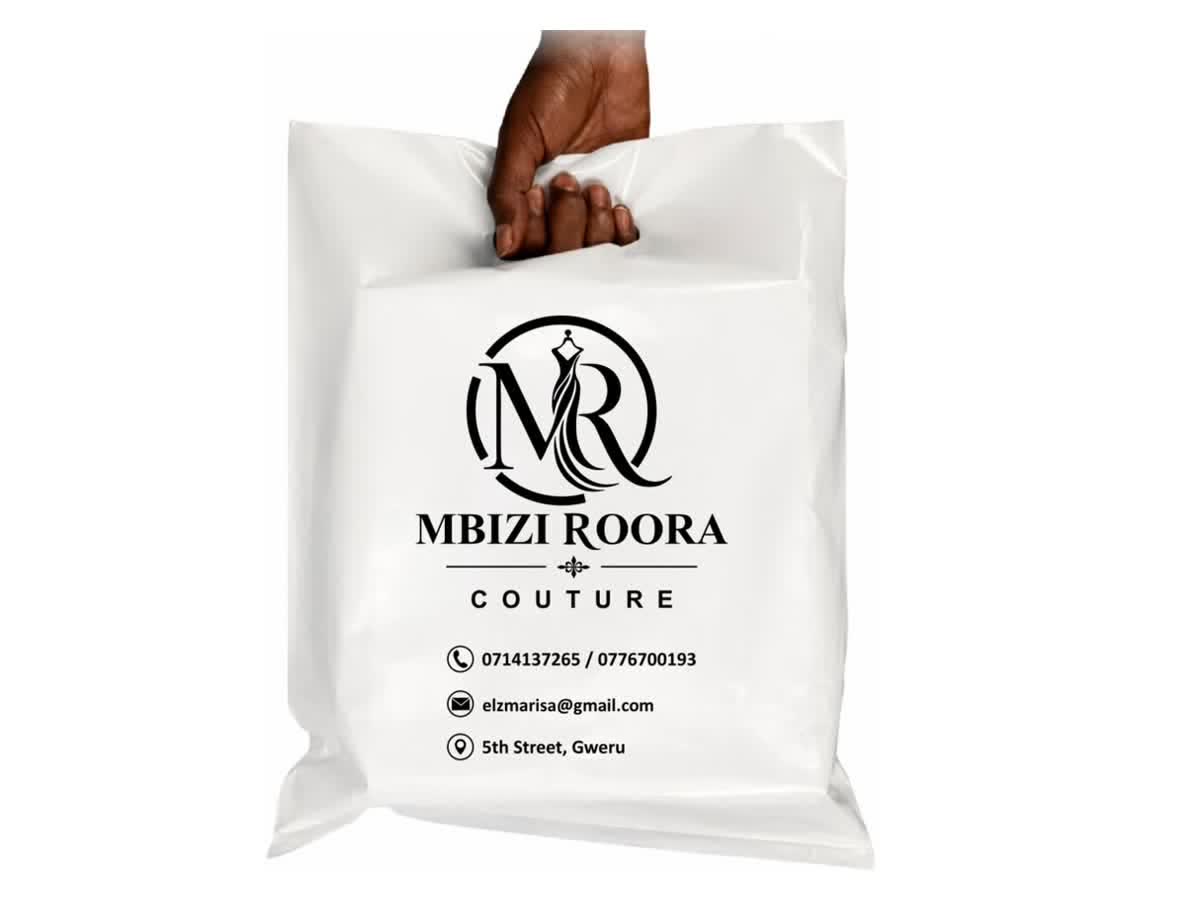 A hand holding a white Mbizi Roora Couture boutique bag printed in black with the label's monogram logo